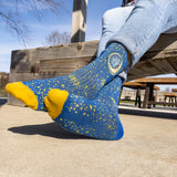 navy blue ribbed sock with yellow star pattern, featuring Oberon Eclipse logo, moon and sun, in full color on the upper portion. Yellow top with QEJA Q
