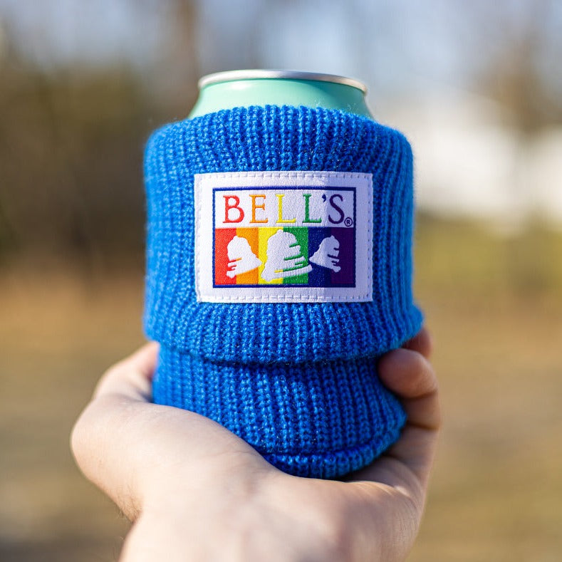 A blue cotton beer sleeve with a rainbow patterned Bell's logo sewn onto it.