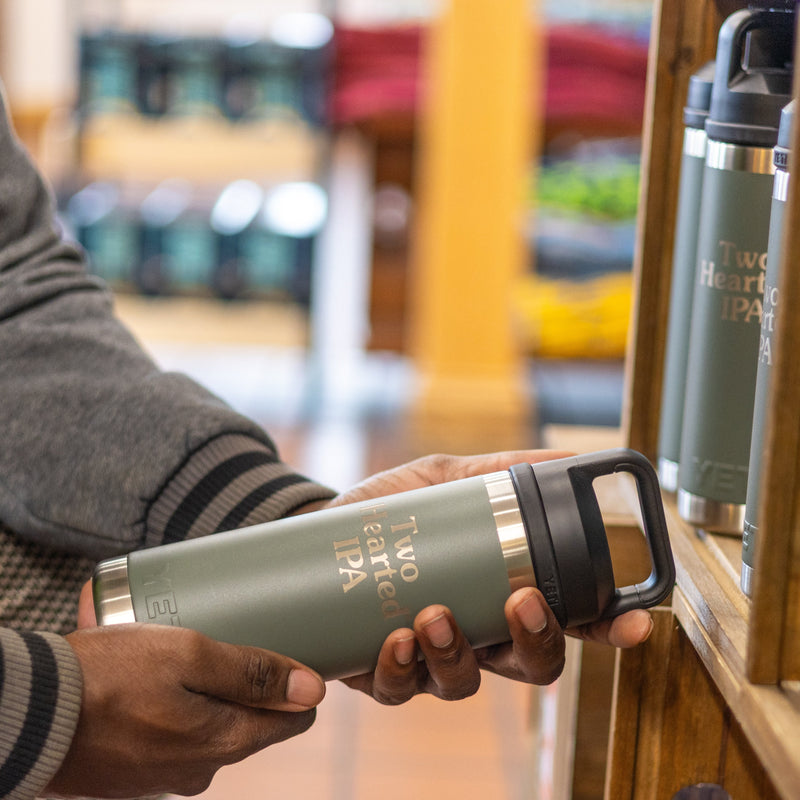 Man holding green Two Hearted Branded Yeti Rambler water bottle, with silver embossed text and a black cap.