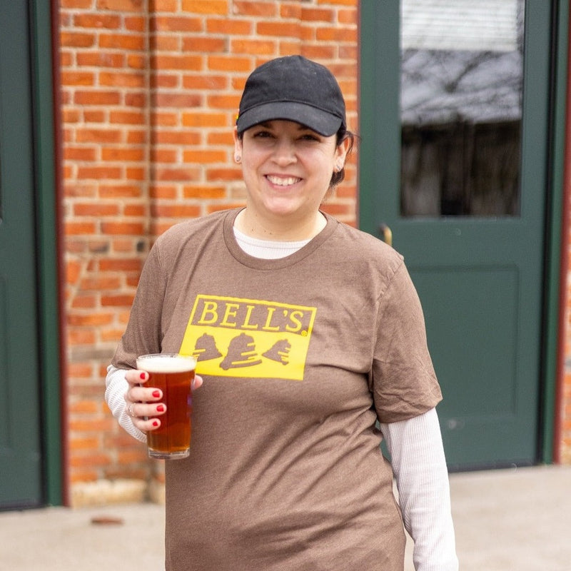Woman wearing brown tee shirt with yellow printed Bell's logo on the front.