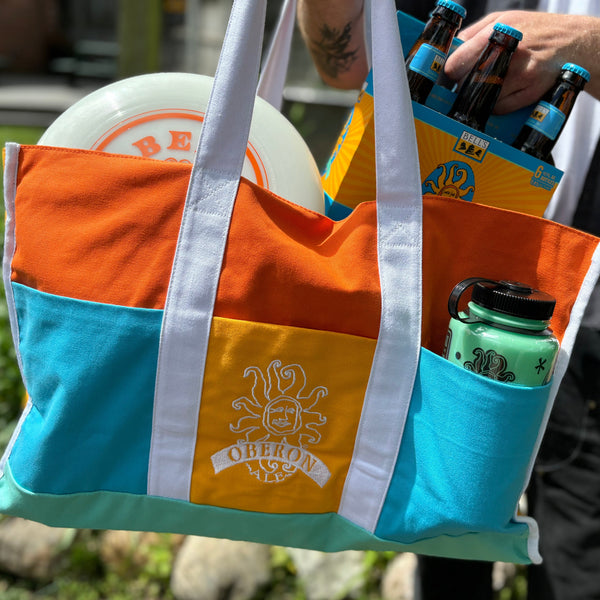 Large canvas tote bag with color block design.  Featuring Oberon colors, Orange, blue and sea green with white straps and accents.  The middle pocket in the center has embroidered white Oberon logo.