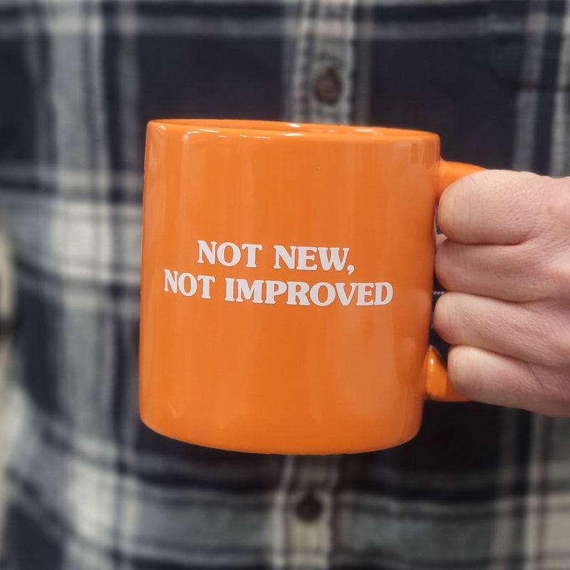 Man holding orange Two Hearted branded coffee mug with "Not new, Not Improved" in white text.
