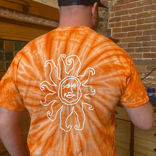 Back view of orange tie dye tee shirt with a large white outline Oberon sun logo.