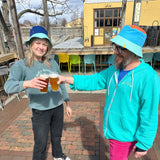 A reversible bucket hat with Oberon tag , teal brim, blue base and orange top on one side. On the other is an Eclipse tag, teal brim, dark blue base and yellow top.
