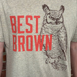 A close-up of a heather light brown t-shirt featuring a graphic print of a brown owl and the text 'BEST BROWN' in red