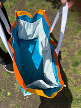 Large canvas tote bag with color block design. Featuring Oberon colors, Orange, blue and sea green with white straps and accents. Inside view of blue liner and white mesh side pockets on 3 of 4 sides on liner, and zipper pocket on 4th side.