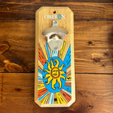 steel bottle opener mounted to wooden plaque featuring Oberon Sun Burst design against wood grain background. Featuring Oberon in white text above opener, with an Oberon sun logo replacing the "O" in the word Oberon