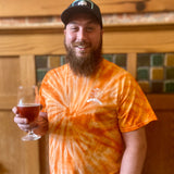 Orange tie dye tee shirt with a white outline Oberon sun logo on the pocket area.