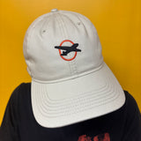 An off white baseball cap with a Flyover logo, black airplane logo inside an orange circle on the front