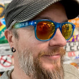 Sunglasses with transparent blue rims and orange lenses, with Oberon text and logo on the temple exterior.