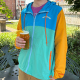 Multicolor windbreaker, teal and blue front of jacket, yellow sleeves, orange drawstring. Oberon written out on the front in a curved text.