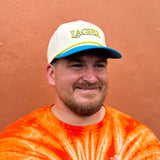WHITE BASE HAT WITH BLUE BILL AND YELLOW PUFFY EMBROIDERED LAGER ON THE FRONT, WITH BLUE OUTLINE  AND YELLOW ROPE ACROSS BILL.