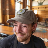 Olive twill baseball cap with embroidered circular Hopslam logo patch sewn onto the center front.