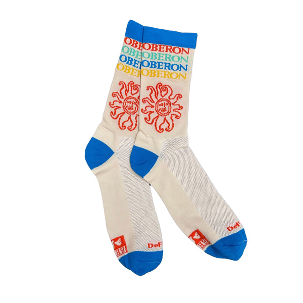 A pair of cream socks with a blue toe, blue heel, and blue trim at the opening. The socks feature the Oberon Ale sun in red and “Oberon, Oberon, Oberon, Oberon” stacked in Red, Teal, Blue, and Yellow. The Bell’s logo in red lives on the bottom of the sock close to the toe.   