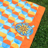Orange framed circular patterns with alternating colors, light and dark blues as well as gold and orange. Underside is full blue. Oberon logo large center placement at the bottom of blanket.