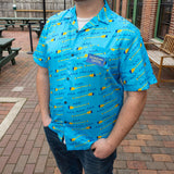 bright blue short sleeve button up shirt with pattern of blue waves and yellow and blue oars. Blue patch on front pocket with yellow embroidered "Lager For the Lakes" logo