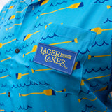 bright blue short sleeve button up shirt with pattern of blue waves and yellow and blue oars. Blue patch on front pocket with yellow embroidered "Lager For the Lakes" logo