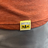 Close-up of a yellow Bell's brand fabric tag sewn onto the hem of an rust red heathered t-shirt