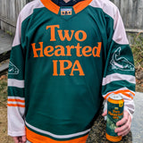 Person wearing a green, white, and orange custom hockey jersey with 'Two Hearted IPA' printed on the front, holding a matching beer can. in white printed on both sleeves a cartoon fish.
