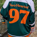 A person viewed from behind wearing a green, white, and orange hockey-style jersey with 'Two Hearted 97' printed on the back.