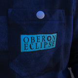 blue plaid flannel shacket with light blue embroidered patch with Oberon Eclipse text logo on pocket.