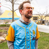 blue baseball jersey with golden sleeves and highlights, orange buttons, and a full color Oberon sun patch on pocket with additional 92 patch beneath.
