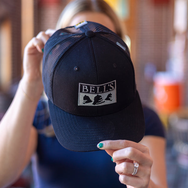 Black trucker cap with twill front and mesh back. Features silver Bell's embroidered logo on the front.
