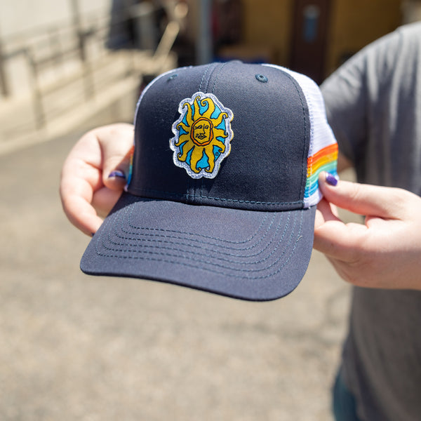 Navy blue trucker hat with white net backing with 4 color stripes on the sides, orange, yellow, green, and blue.  Also features full color Oberon sun patch.