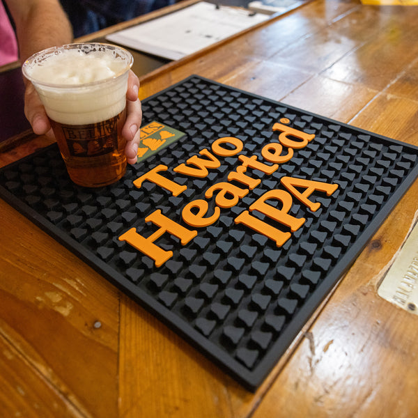 Black bar mat with bell texture featuring small Bell's logo in orange and green top center and Two Hearted Ale in orange large at the bottom center.