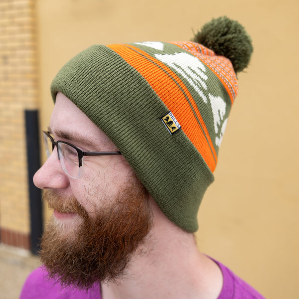 Sage green knit cap with orange knit accents and sage green pom. Features light Bell's logo pattern in the middle. Small Bell's tag sewed onto the folded base of the cap.