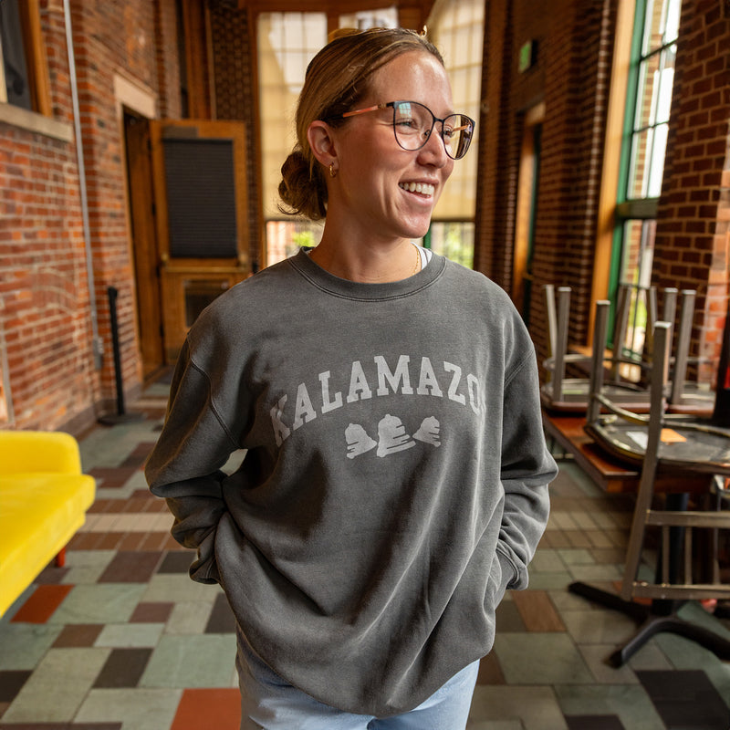 charcoal color crewneck sweater with Kalamazoo printed in gray across the front in college style.  featuring gray Bell's logo bells beneath