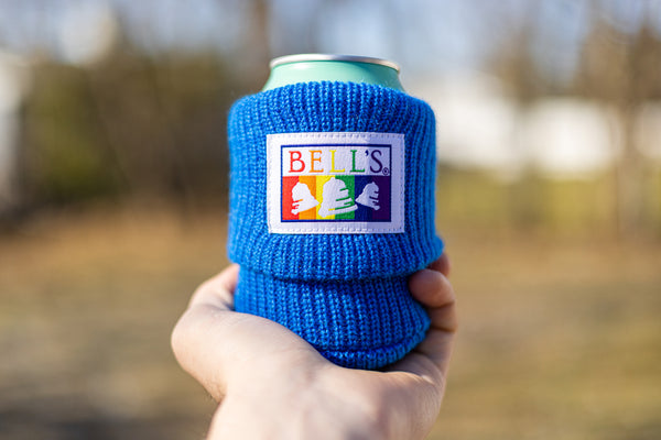 A blue cotton beer sleeve with a rainbow patterned Bell's logo sewn onto it.