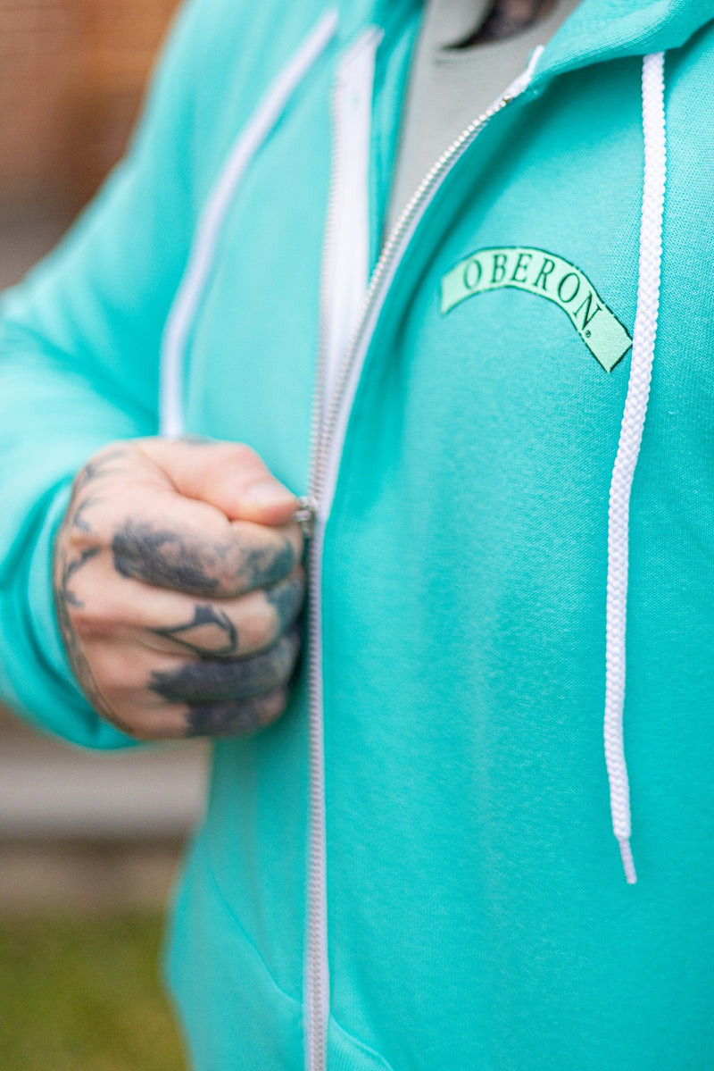 Teal zip up hoodie hoodie, small teal Oberon banner on the pocket are of the front.