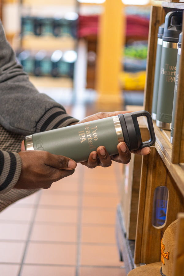 Man holding green Two Hearted Branded Yeti Rambler water bottle, with silver embossed text and a black cap.