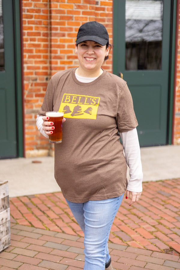 Woman wearing brown tee shirt with yellow printed Bell's logo on the front.
