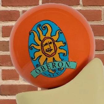 Zoom in of the Bell's Brewery beer tap handle with a orange globe with the Bell's Oberon logo, in front of a brick wall.
