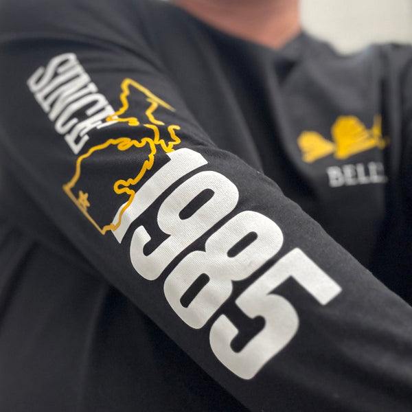 black long sleeve tee shirt featuring yellow Bells logo with white text "Bells" beneath on pocket.  "Since 1985" printed in white on right sleeve with outline of Michigan in yellow.  A yellow star is in place of Kalamazoo on the map.