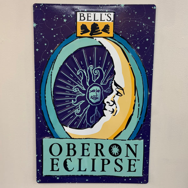 Rectangular tin sign featuring Oberon Eclipse art, including light blue stars, constellations, and dotted lines on a dark blue background. Bell's logo in black, white, and yellow is top center. Oberon Eclipse moon in varying shades of blue and yellow with Oberon outline inside. Oberon Eclipse in black on a light blue background at the bottom.