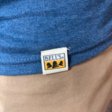Close-up of a blue heathered t-shirt hem with a sewn-on white brand patch reading BELL'S