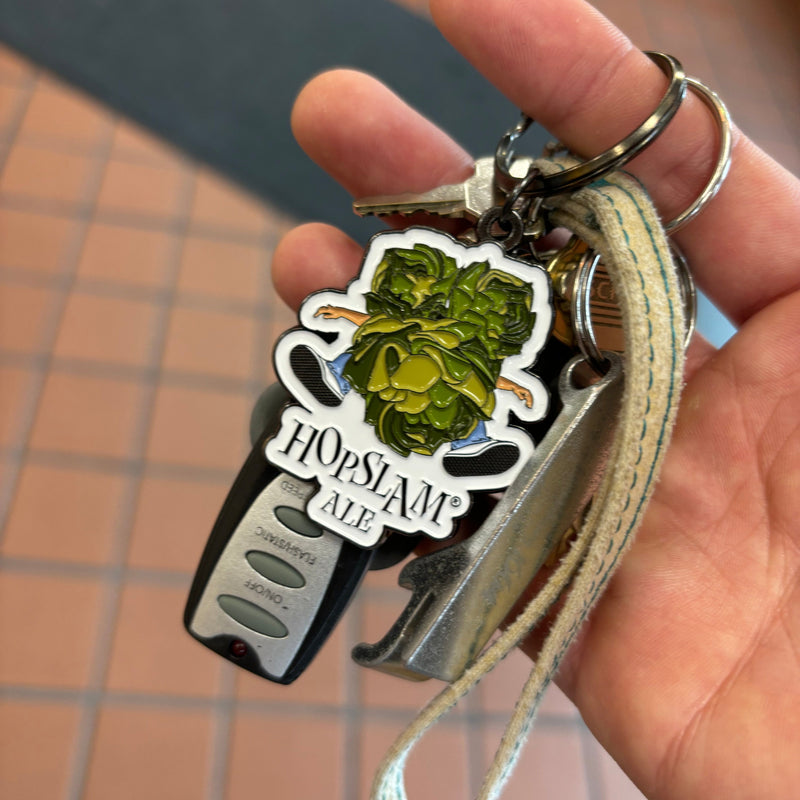 metal keychain with full color enamel Hopslam logo, a man crushed beneath a hop cone