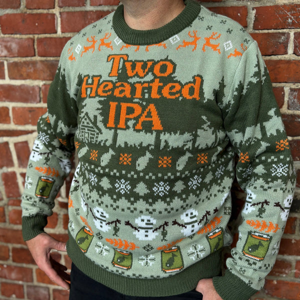 Person wearing a 'Two Hearted IPA' themed sweater "UGLY" HOLIDAY SWEATER, base color light green with dark green forest pattern and fishing images in orange with white snowmen.  Bold orange Two Hearted IPA logo on chest with dark green outline.