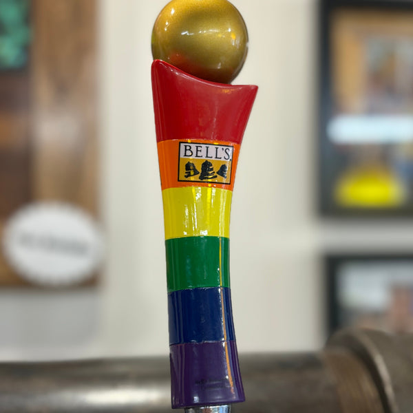 Beer tap handle with rainbow colored stripes (red at the top, orange, yellow, green, blue, purple) and a gold sphere on top. Bell's logo featured on orange stripe.