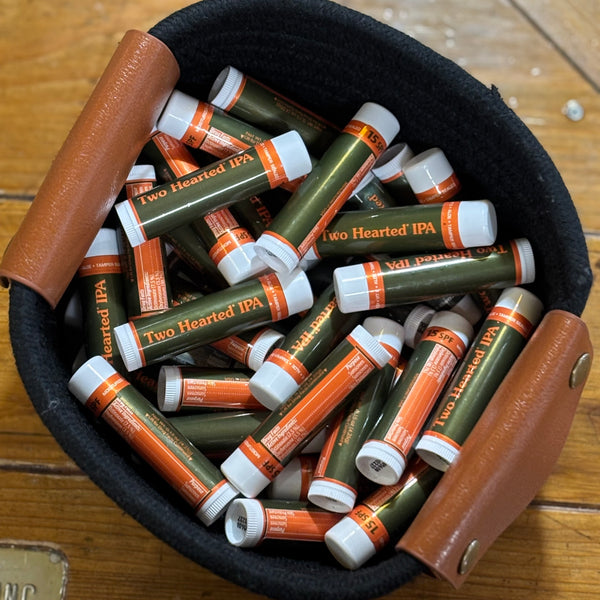 White lip balm tube with Two Hearted IPA text in orange over green background. Backside has orange box with drug facts in white