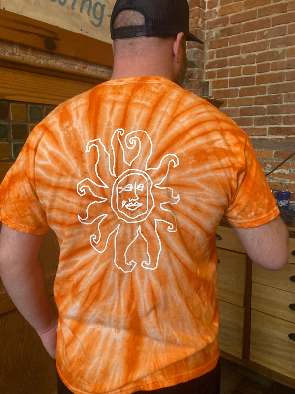 Back view of orange tie dye tee shirt with a large white outline Oberon sun logo.