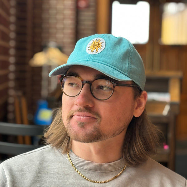 light teal colored dad hat with white oval patch in center with embroidered full color Oberon sun