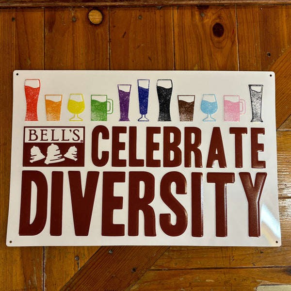White rectangle tin sign with eleven beer glasses filled with liquids of rainbow colors, including (Left to Right), red, orange, yellow, green, purple, blue, black, brown, light blue, pink, and gray. "Celebrate Diversity" and Bell's logo below in maroon.