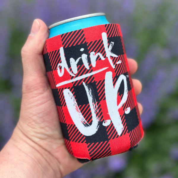 A can sleeve neoprene foam insulator sleeve for 12oz beverage cans. The sleeve is red and black buffalo plaid. The white circular Upper Hand logo is printed on the front. The text 'Drink U.P.' is printed in white across the front.