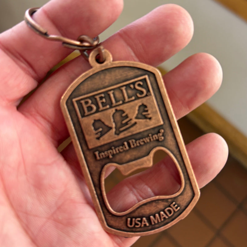 A bottle opener keychain made of a bronze metal with the Bell's logo and the words "Inspired Brewing" and "USA MADE."