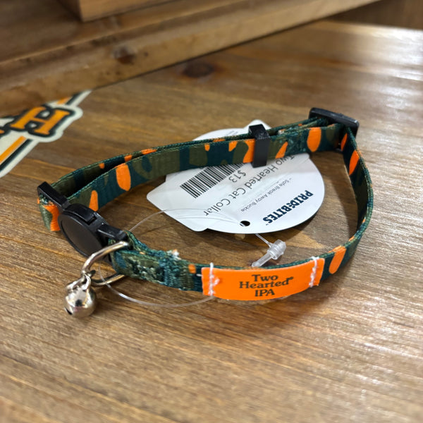 Cat collar with silver bell, featuring Two Hearted branding with green text on orange block at the front. Most of the collar has camo print in same colors.