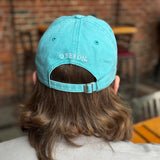 back of light teal colored dad hat with embroidered white lettering over strap reads Oberon.  strap had buckle for adjustment